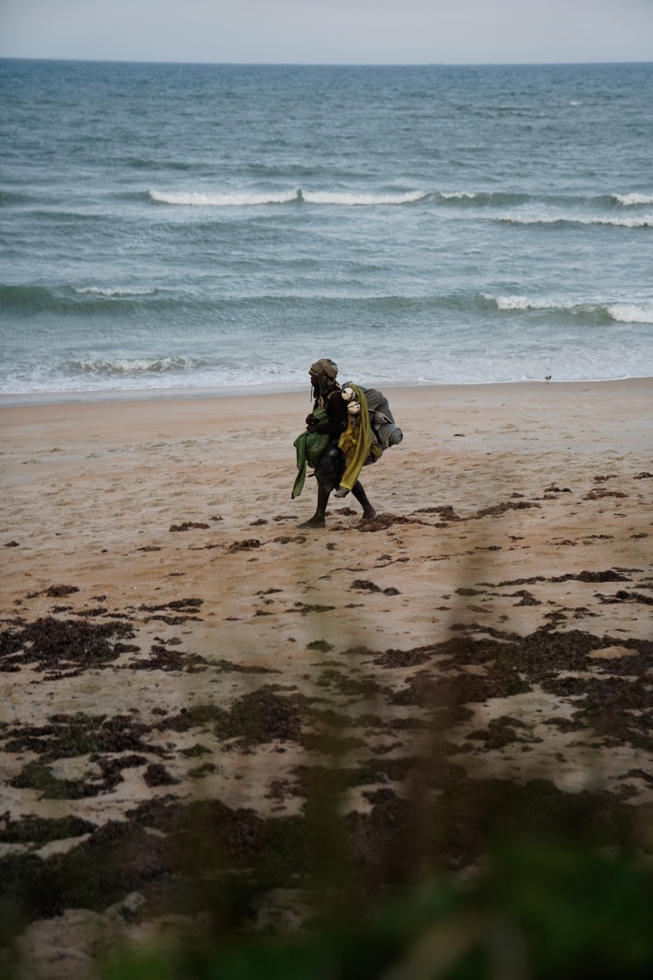 Lone figure walking along a quiet beach beneath layered ocean waves